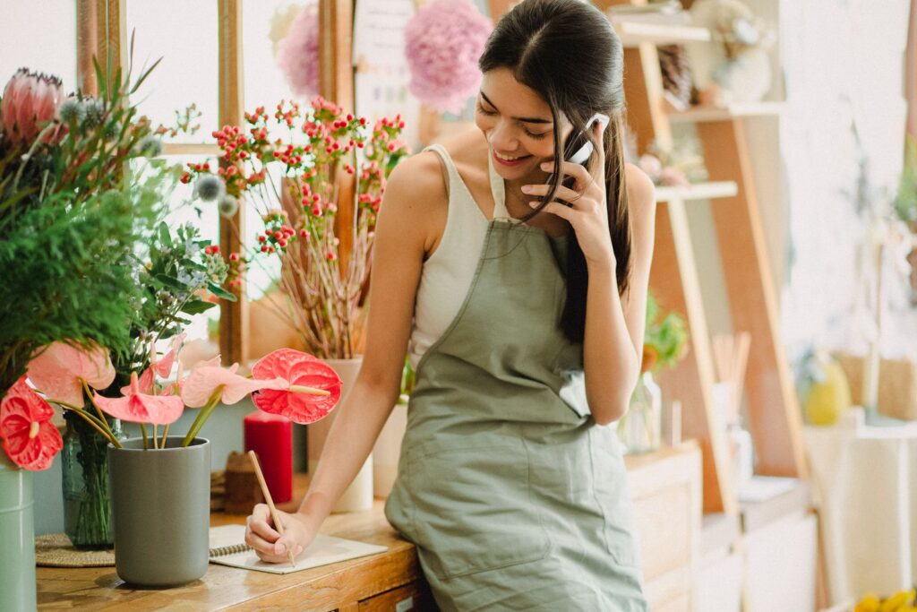 Dueña de una floristería sonriendo mientras atiende una llamada y gestiona su negocio local