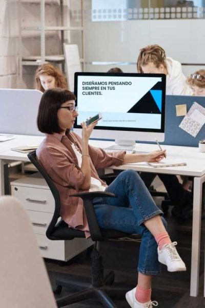 Diseñadora de Sucursal Creativa hablando por teléfono en la oficina, con el mensaje 'Diseñamos pensando siempre en tus clientes' en el monitor